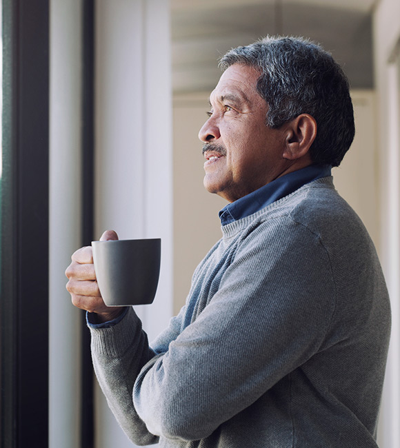 Senior man drinking coffee and looking thoughtfully out of a window in Whitby Canada